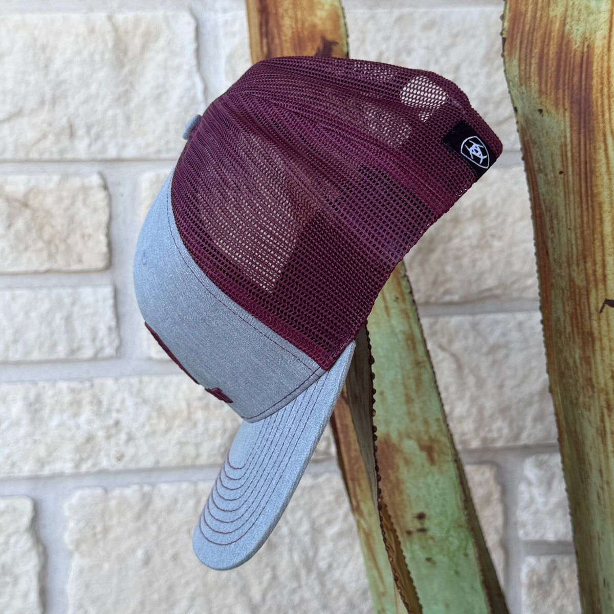A two-tone trucker cap with a maroon mesh back and a light gray fabric brim, 