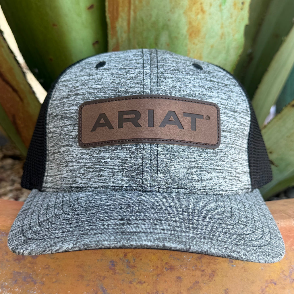 A heather gray trucker hat with black mesh side panels and a brown leather patch on the front that reads ARIAT, 