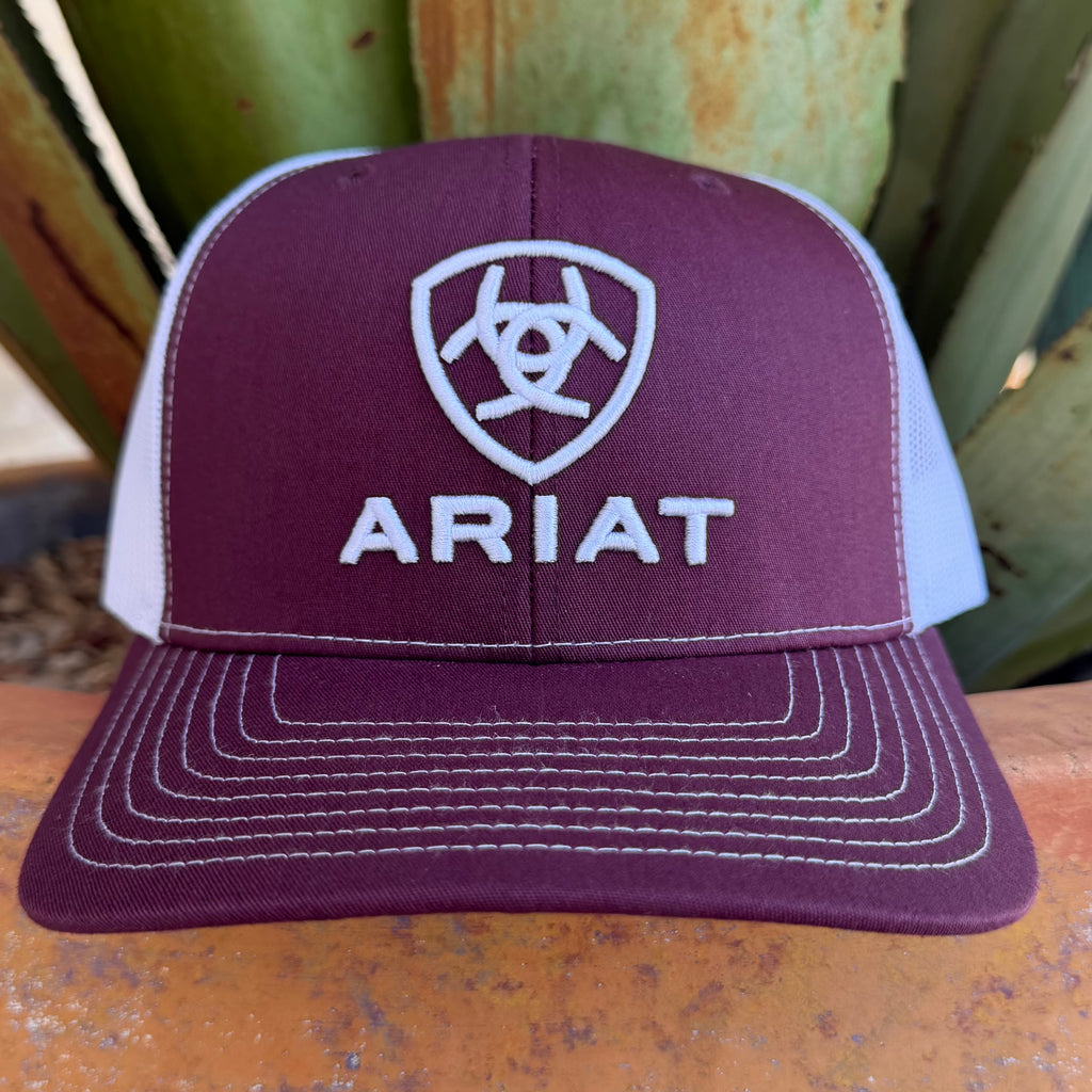 A maroon and white trucker hat with white embroidered Ariat logo and text, 