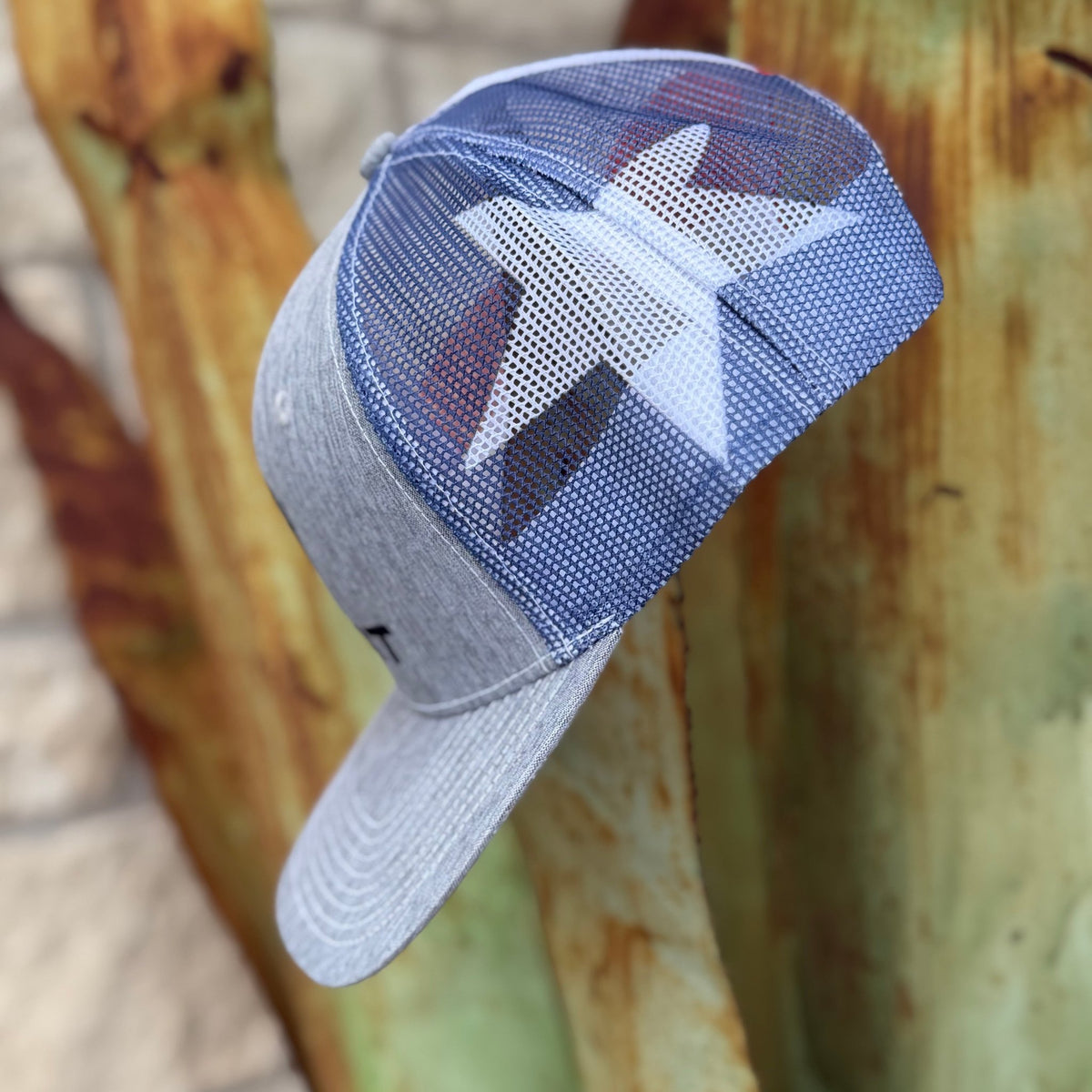 A gray and blue trucker-style cap with a white star graphic on the side mesh panel, photographed outdoors
