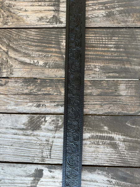 Black leather with edge-to-edge floral scroll tooling, dot edge stitching, and a large engraved silver western buckle with matching keeper — a timeless western belt with deep, handcrafted detail and sharp black-on-silver contrast.