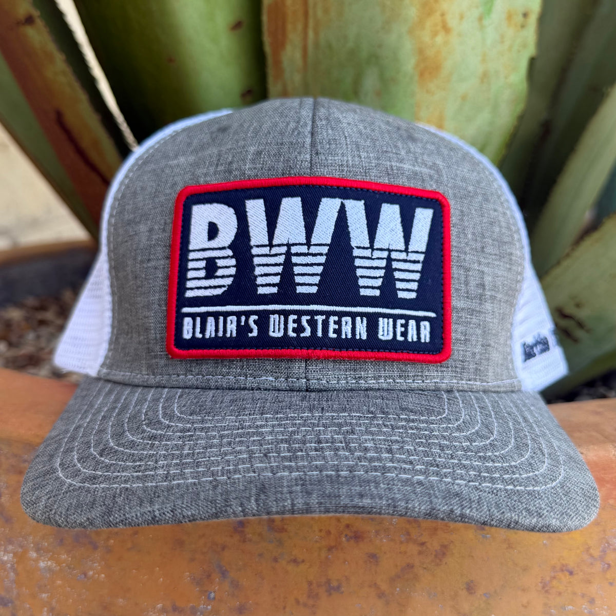 A heather gray and white trucker hat with a prominent rectangular patch on the front that reads 'BWW BLAIR'S WESTERN WEAR'. 
