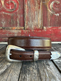 A brown leather belt with a silver-toned western-style buckle and decorative tip, coiled on a rustic wooden surface with a distressed red wooden background.