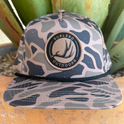 A camouflage trucker hat with a circular 'BURLEBO OUTDOORS' patch on the front, 