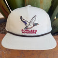 A cream snapback cap featuring an embroidered flying duck logo and the text 'BURLEBO OUTDOORS' in red on the front, with a dark brown band around the crown.