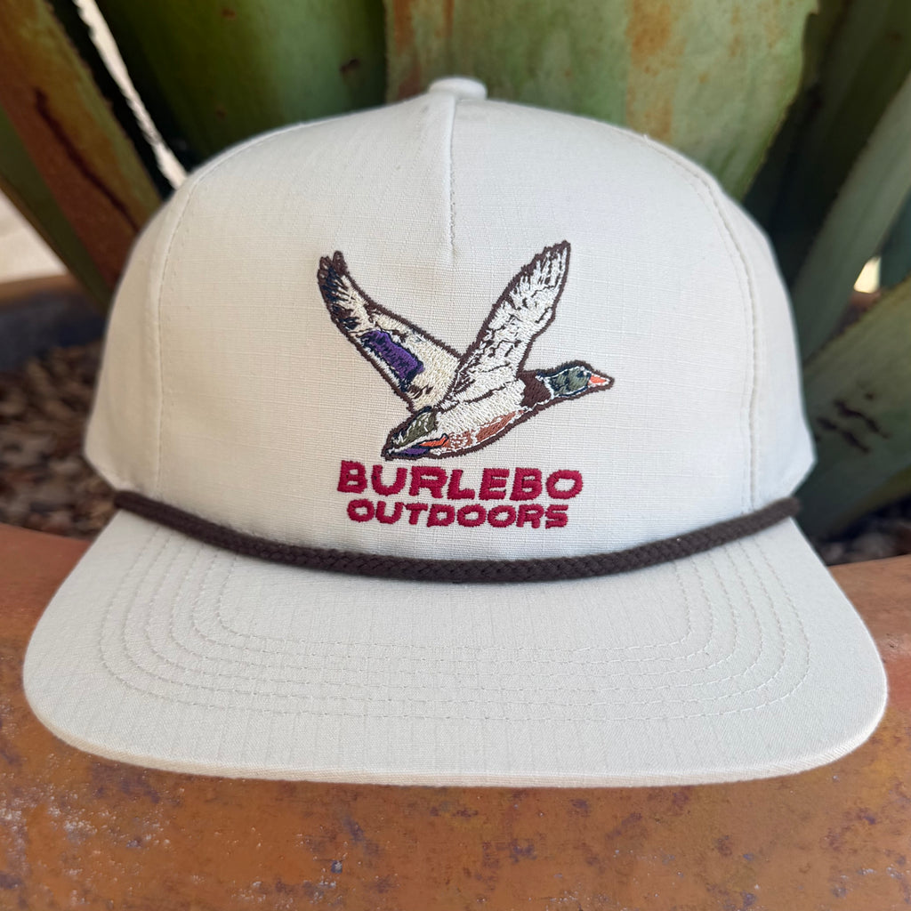 A cream snapback cap featuring an embroidered flying duck logo and the text 'BURLEBO OUTDOORS' in red on the front, with a dark brown band around the crown.