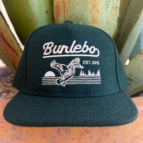 A dark forest green flat-brim cap with white embroidered text reading 'Burlebo' and a duck graphic with 'EST. 2015' on the front,
