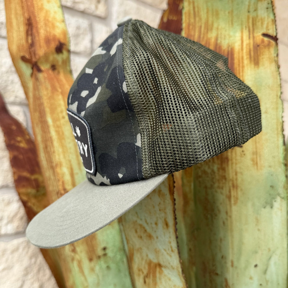 A camouflage trucker cap with a flat light gray/olive brim