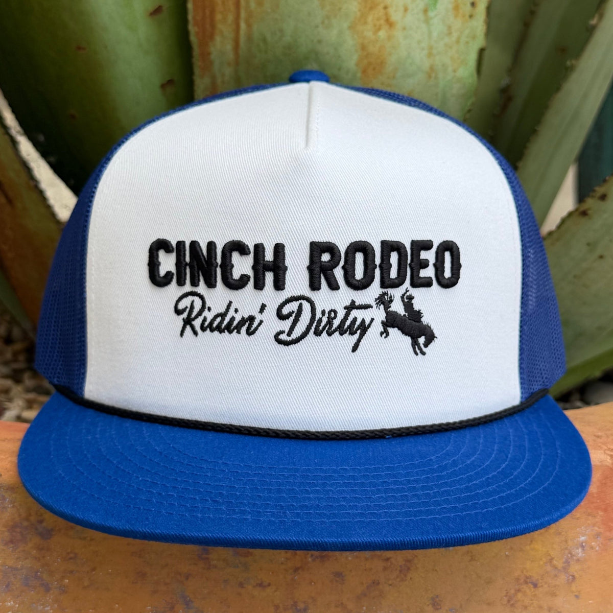 A blue and white trucker hat with black embroidered text reading 'CINCH RODEO Ridin' Dirty' and a cowboy riding a bucking horse