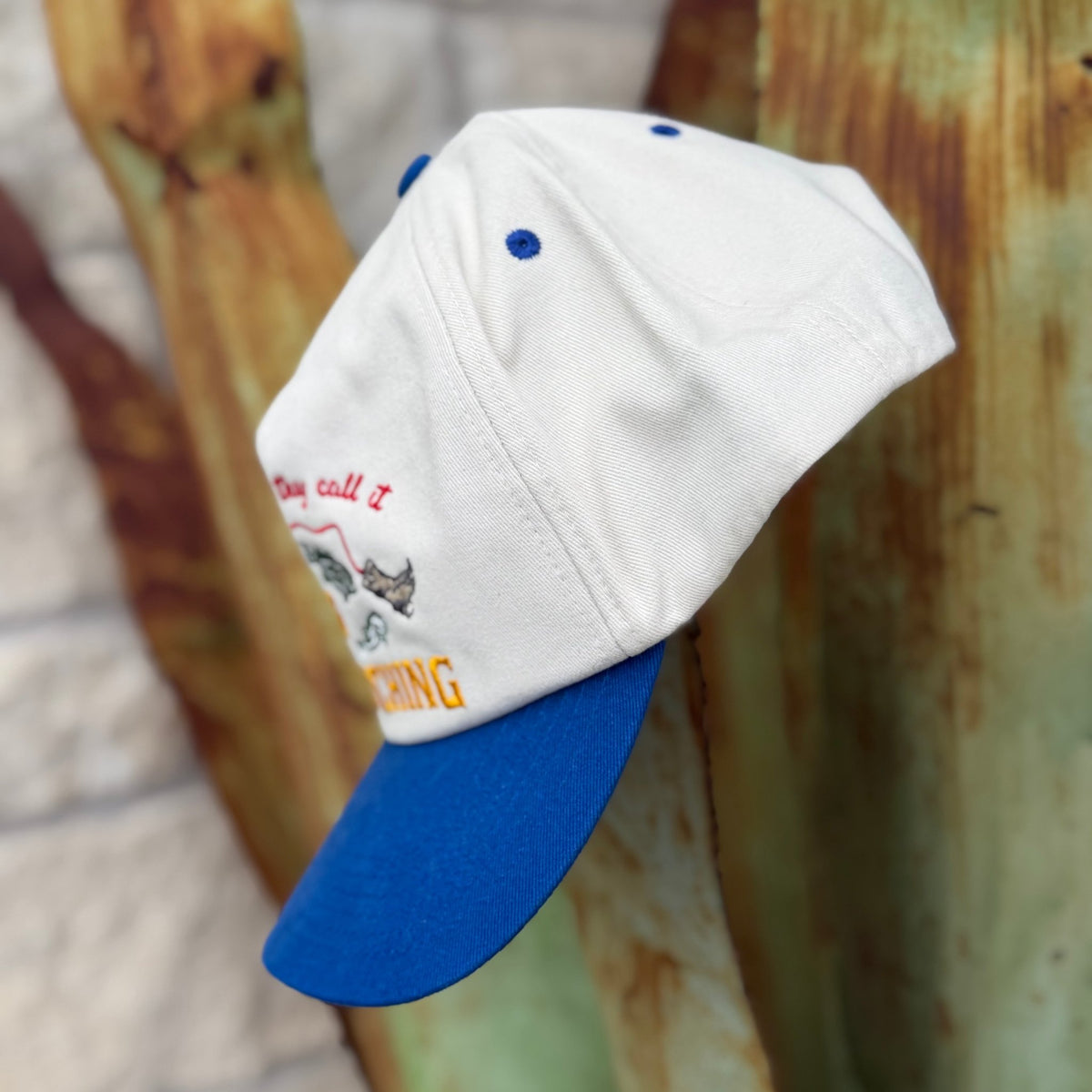 A clean structured five-panel silhouette with a pre-curved blue bill and breathable mesh back. The embroidered fishing graphic and bold lettering run across the front in a natural, blue, and yellow colorway — fun, detailed, and built to hold up wear after wear. Snapback closure at the back for a dialed-in fit.