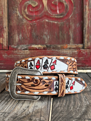 A tooled leather belt with a silver buckle, featuring a western design with white stitching and printed playing card motifs including four aces, displayed on a rustic wooden surface in front of a red wooden door.