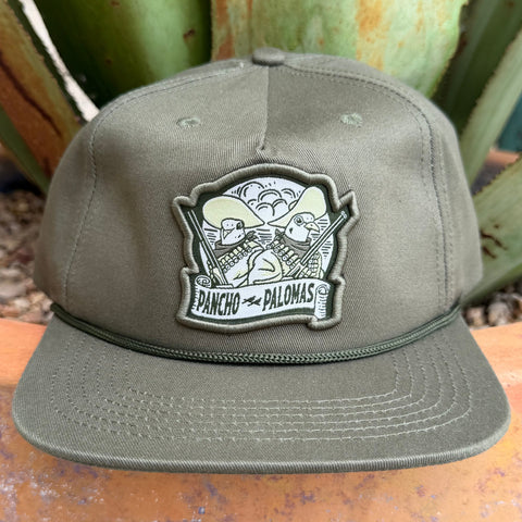 An olive green snapback cap with a custom embroidered patch reading 'PANCHO PALOMAS' featuring two doves with rifles