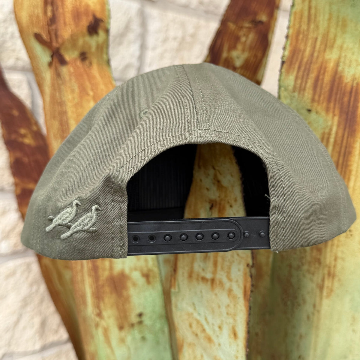 An olive green baseball cap shown from the back, featuring two embroidered birds on the left side of the crown and a black adjustable strap