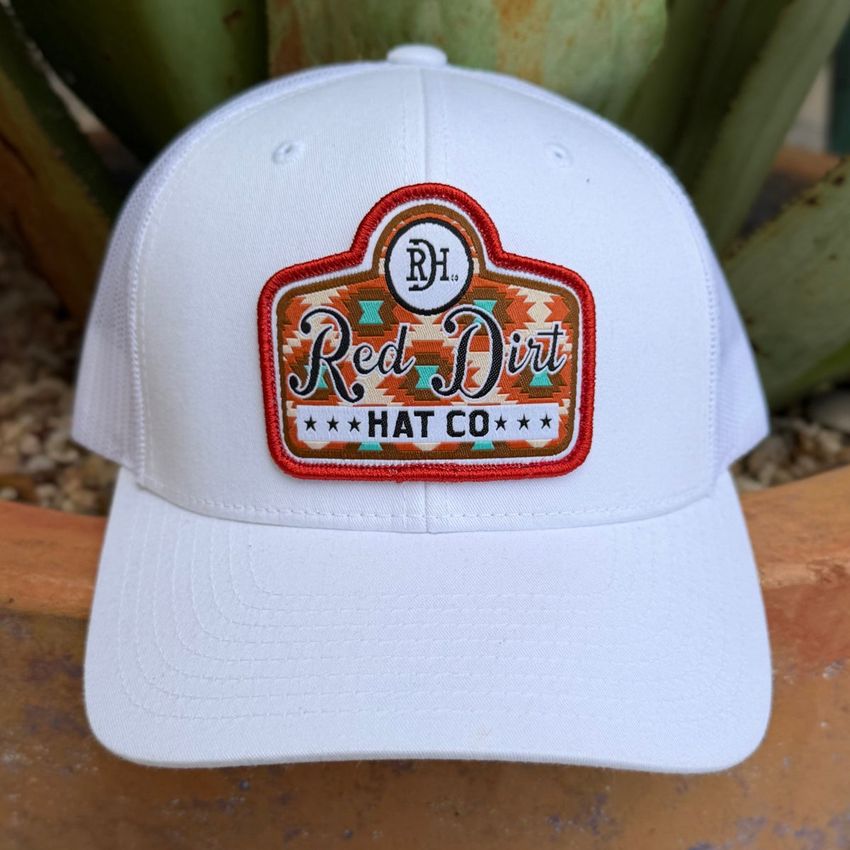 Men's White cap with aztec Red Dirt Hat Co. Logo at the front in the colors red-orange, brown , and turquoise  - it has a an adjustable snapback strap on the back for adjustable fit 