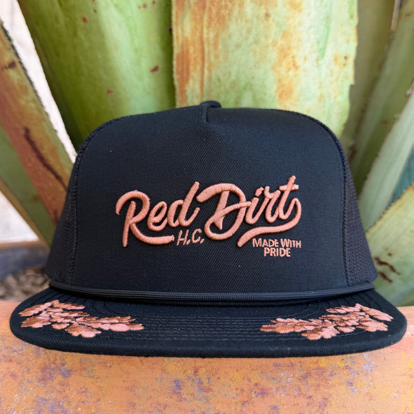 A black trucker-style cap with a flat brim, featuring rose gold embroidered 'Red Dirt H.C.