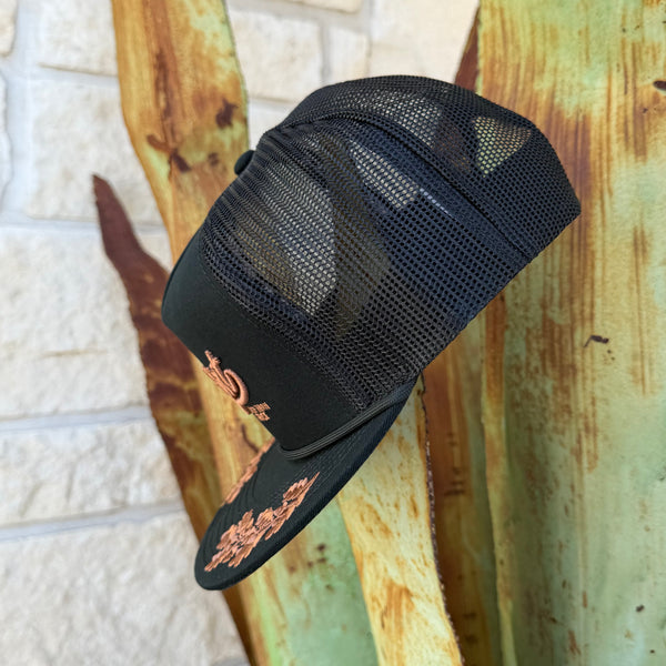 A black trucker-style cap with a mesh back and rose gold embroidered floral details on the bri
