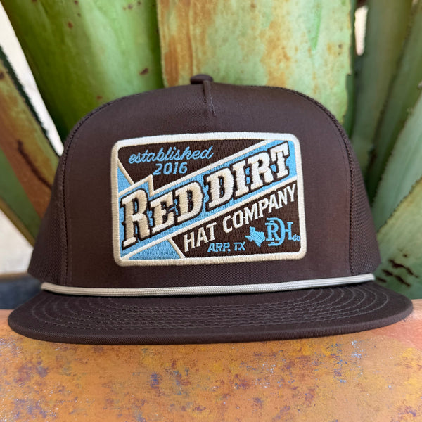 A dark brown snapback cap with a large embroidered front patch reading 'Red Dirt Hat Company' and 'established 2016 ARP, TX'