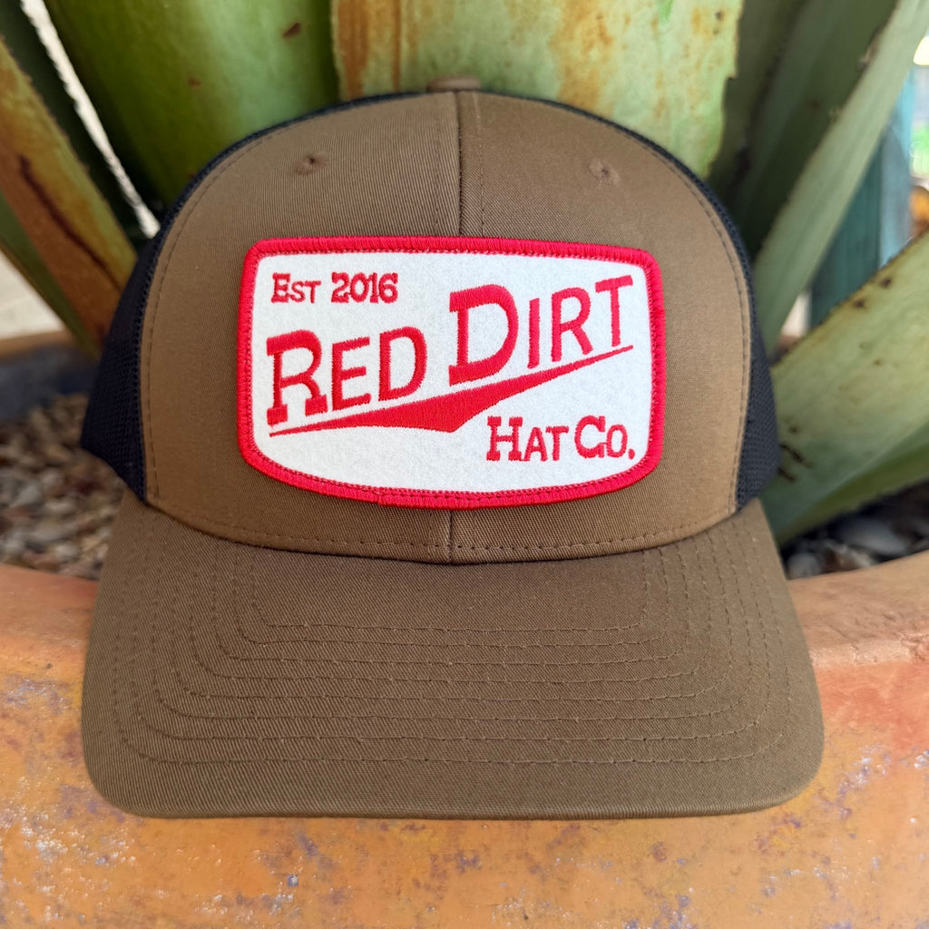 A brown and black trucker hat with a large front patch reading 'RED DIRT Hat Co. Est 2016',