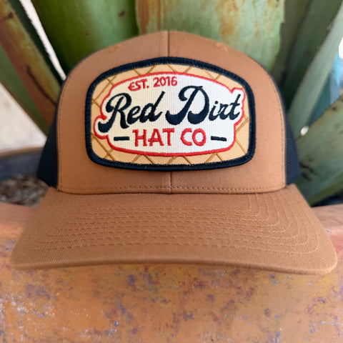 A burnt orange trucker hat with a black mesh back and a large embroidered front patch reading 'Red Dirt Hat Co' and 'Est. 2016', 
