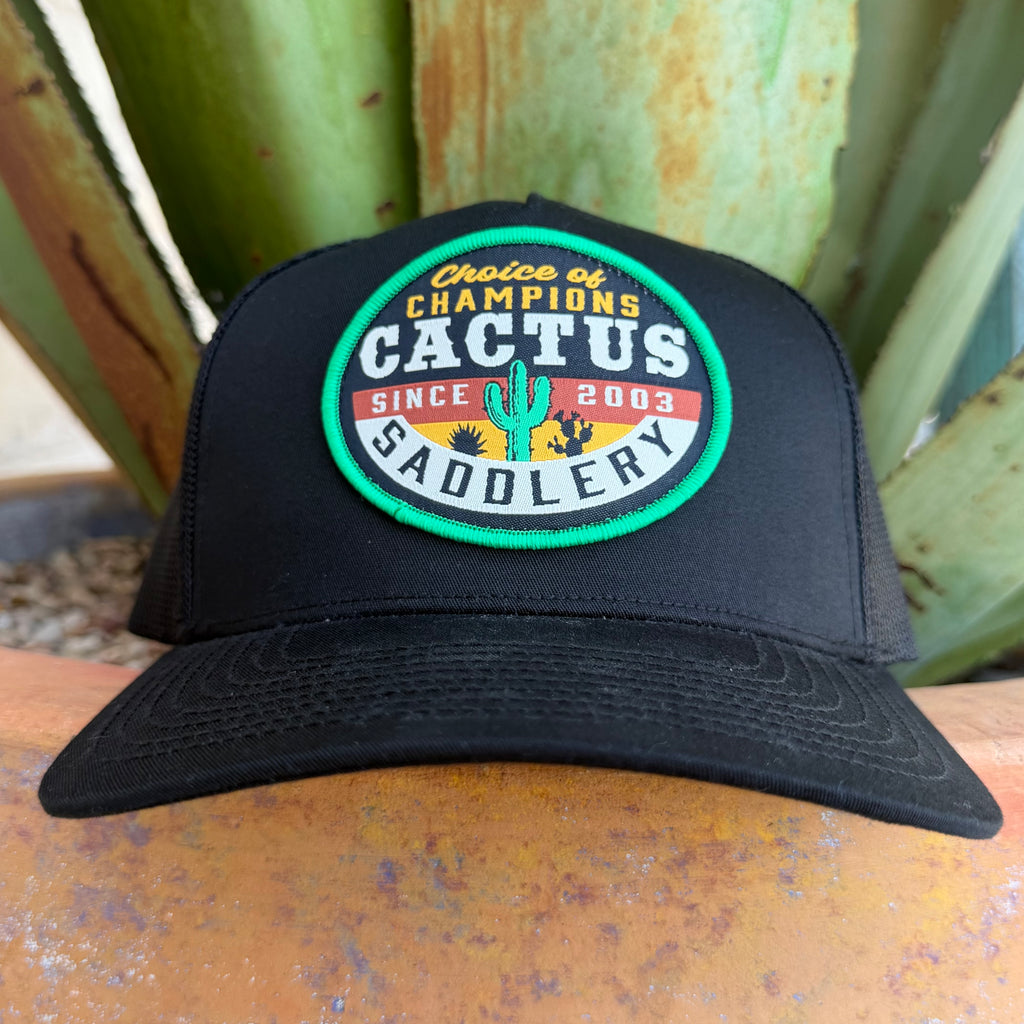 A black trucker-style cap with a circular embroidered patch reading 'Choice of Champions Cactus Saddlery Since 2003,' 