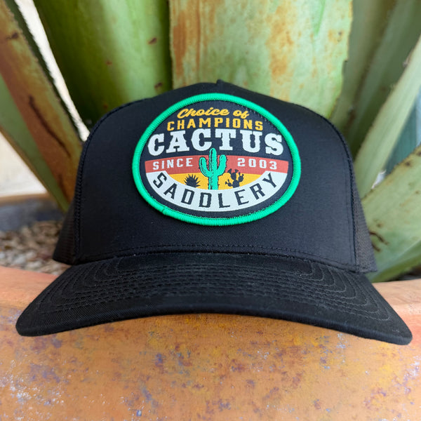 A black trucker-style cap with a circular embroidered patch reading 'Choice of Champions Cactus Saddlery Since 2003,' 