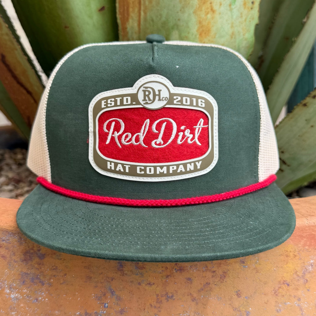 A green and cream trucker hat with a red embroidered logo patch reading 'Red Dirt Hat Company' and a red rope detail on the brim