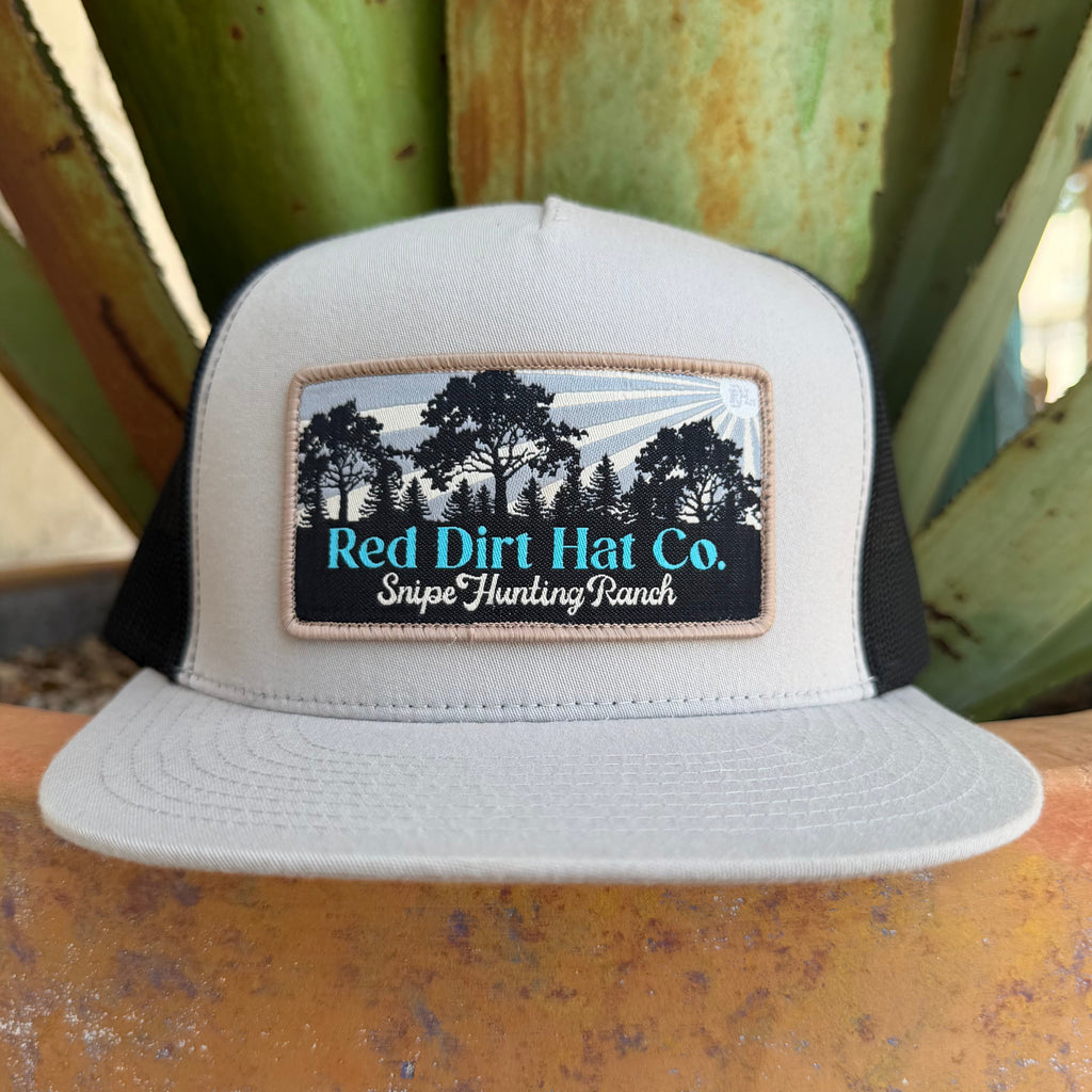 A light gray and black trucker hat with a front patch reading 'Red Dirt Hat Co. Snipe Hunting Ranch' and a tree graphic