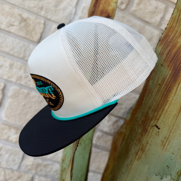 Men's Red Dirt Hat Co. Turquoise &amp; Gold Logo Cap— RDHC-556 Clean contrast, bold logo. This Red Dirt Hat Co. trucker pairs a cream structured front and mesh back with a sharp black brim and teal rope cord — anchored by a standout oval patch that looks intentional from every angle