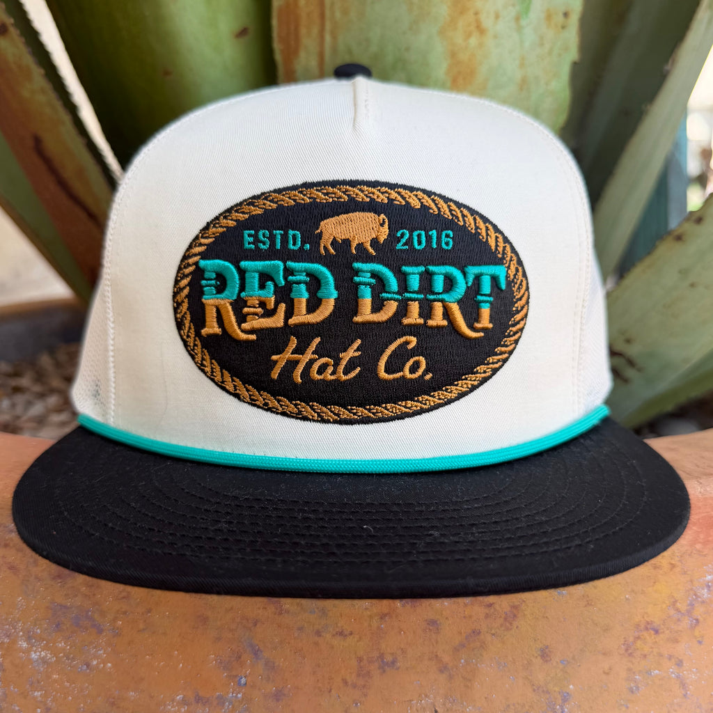 Men's Red Dirt Hat Co. Turquoise &amp; Gold Logo Cap— RDHC-556 Clean contrast, bold logo. This Red Dirt Hat Co. trucker pairs a cream structured front and mesh back with a sharp black brim and teal rope cord — anchored by a standout oval patch that looks intentional from every angle