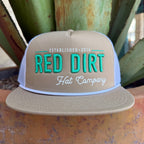 A beige trucker hat with turquoise and white embroidered text reading 'RED DIRT Hat Company' and 'ESTABLISHED 2016', 