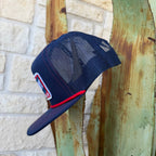 This Red Dirt Hat Co. trucker keeps it classic with a structured navy front, breathable mesh back, and a bold embroidered patch that does all the talking. The red rope accent cord along the brim adds just enough detail to set it apart from every other cap on the rack.