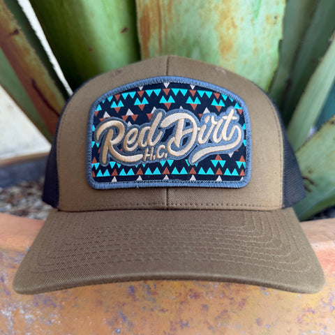 A cap with a curved brim and a front patch reading 'Red Dirt HC' in beige script over a turquoise, black, and brown geometric pattern.