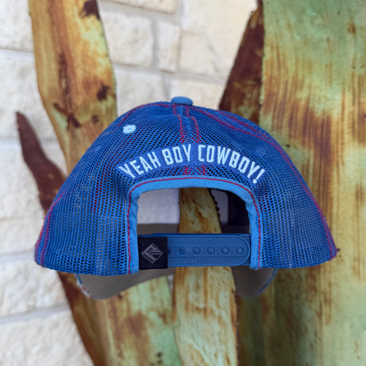 A blue mesh trucker cap with red stitching and white text reading 'YEAH BOY COWBOY!' on the back, 