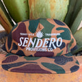 A camouflage cap with white embroidered text reading 'TEXAS USA TRADEMARK SENDERO PROVISIONS CO.' and the Sendero logo  on the front, 
