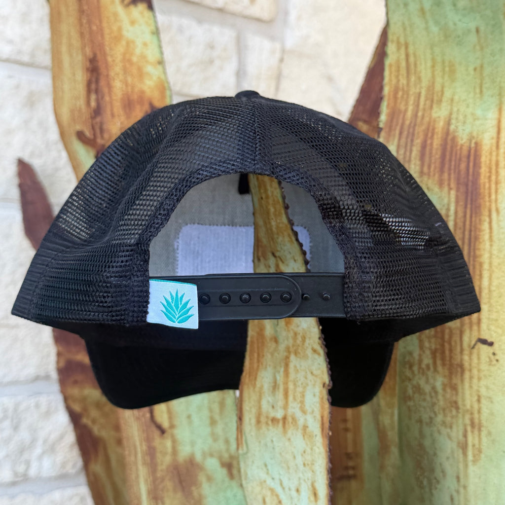 Black trucker-style cap shown from the back, featuring a black mesh back, black adjustable snap strap, and a small white brand tag with the Sendero logo. 