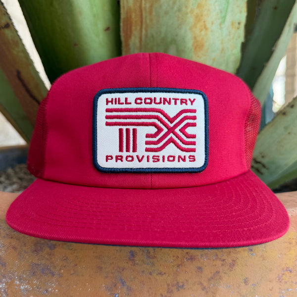 A bright red cap with a white rectangular front patch reading 'HILL COUNTRY PROVISIONS' and a red logo, 