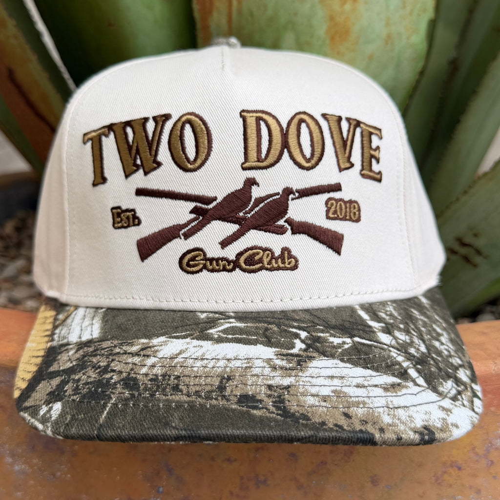 A white snapback cap with a camouflage-patterned brim, featuring 'TWO DOVE Gun Club' embroidered on the front with two birds and crossed rifles.