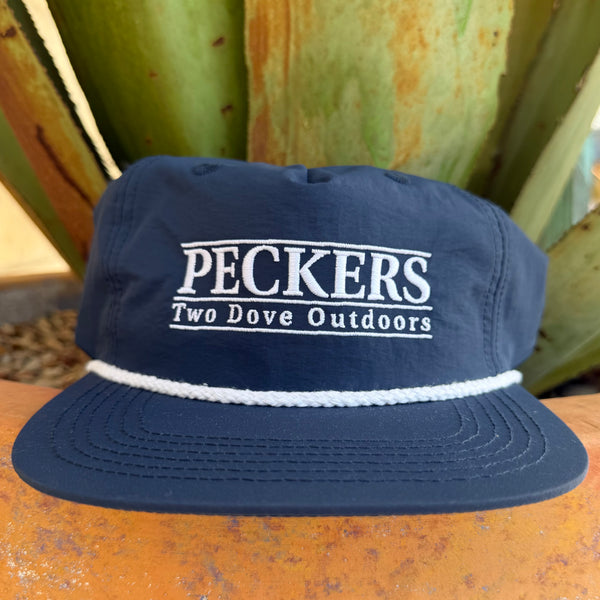 A navy blue snapback cap with 'PECKERS Two Dove Outdoors' embroidered in white on the front