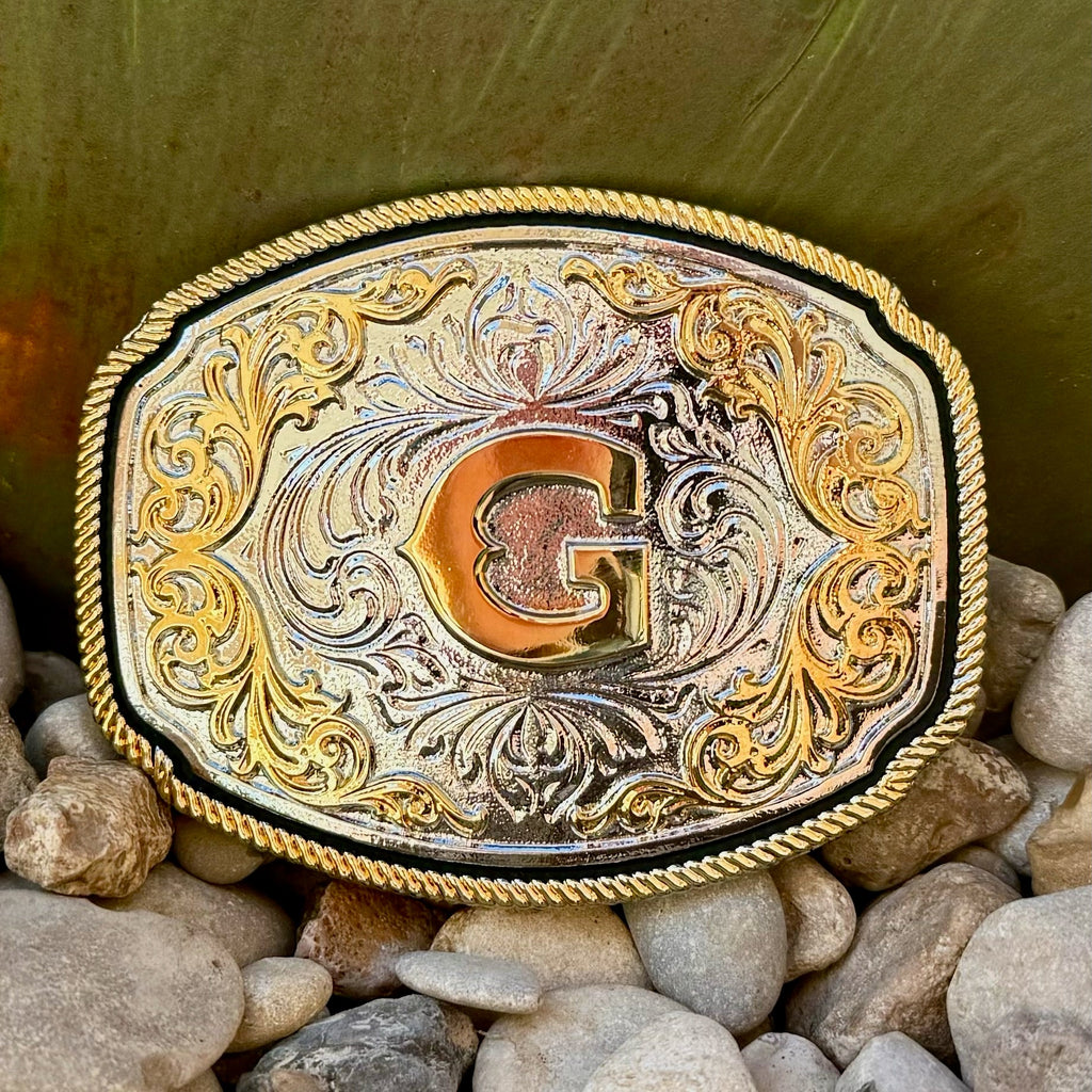 Montana Silversmiths Belt Buckle in silver and gold, featuring detailed engravings and filigree embellishments with a central gold initial - A1047G. Available at Blair's Western Wear, Marble Falls, TX.
