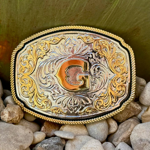 Montana Silversmiths Belt Buckle in silver and gold, featuring detailed engravings and filigree embellishments with a central gold initial - A1047G. Available at Blair's Western Wear, Marble Falls, TX.