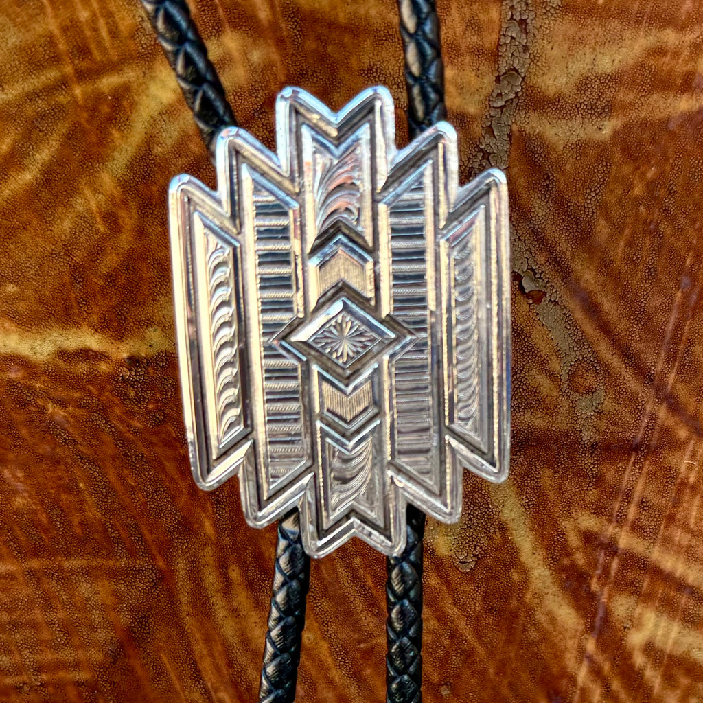 Montana Silversmiths bolo tie Aztec style in silver, intricately engraved geometric slide with layered detailing, with black braided leather cord and polished silver tips - BT6162. Available at Blair's Western Wear, Marble Falls, TX.