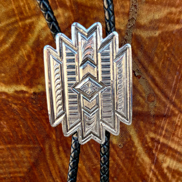 Montana Silversmiths bolo tie Aztec style in silver, intricately engraved geometric slide with layered detailing, with black braided leather cord and polished silver tips - BT6162. Available at Blair's Western Wear, Marble Falls, TX.