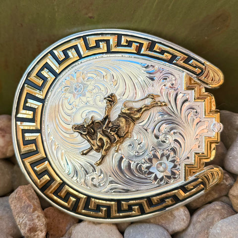 Montana Silversmiths buckle silver/gold horseshoe bull rider buckle in two-tone finish, featuring raised bull rider detailing, with durable Greek-key border engraving – 52810-160. Available at Blair's Western Wear, Marble Falls, TX.