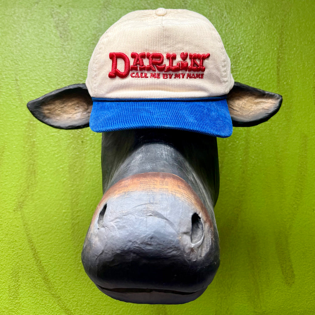 Sendero Provisions Co. Darlin cap in tan crown with blue bill, puff-embroidered “Darlin – Call Me By My Name,” with breathable mesh back and adjustable snapback closure – CAP CALL MY NAME EMB. Available at Blair's Western Wear, Marble Falls, TX.