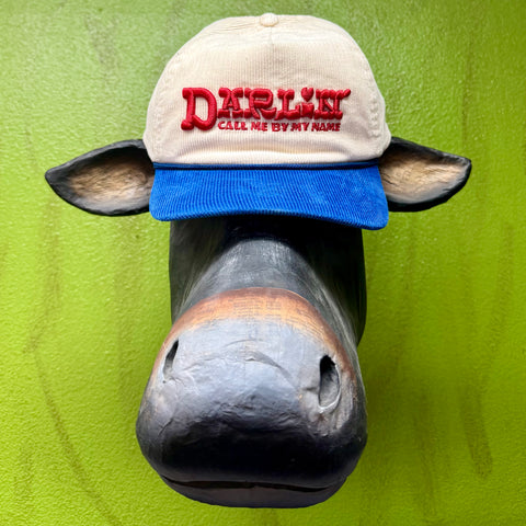Sendero Provisions Co. Darlin cap in tan crown with blue bill, puff-embroidered “Darlin – Call Me By My Name,” with breathable mesh back and adjustable snapback closure – CAP CALL MY NAME EMB. Available at Blair's Western Wear, Marble Falls, TX.