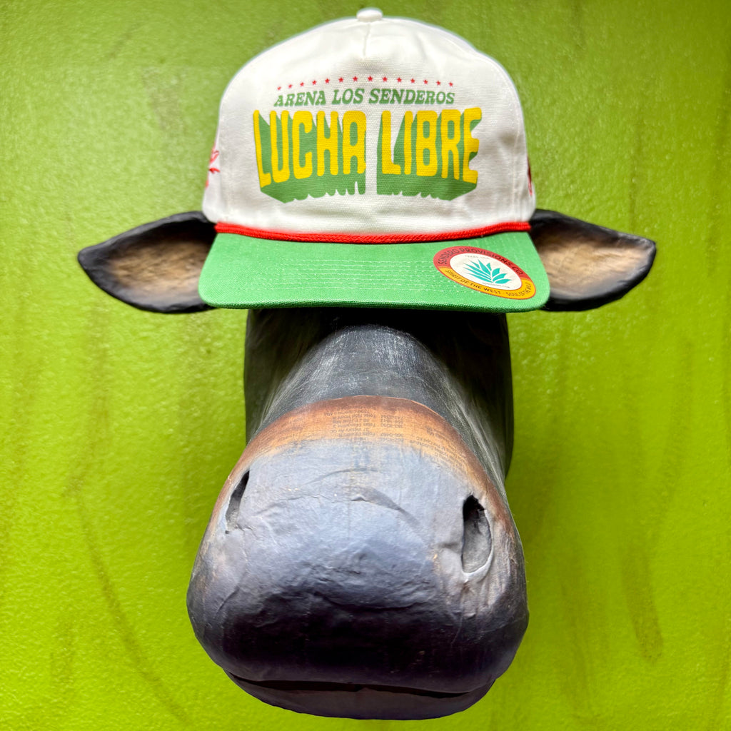 Sendero Provisions Co. Lucha Libre cap in natural, green, and yellow, featuring “Arena Los Senderos” front design, red rope trim, and adjustable snapback closure – LUCHA LIBRE. Available at Blair’s Western Wear, Marble Falls, TX.