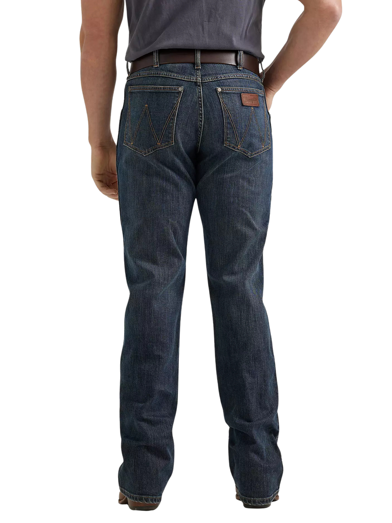 Rear view of a person wearing dark blue denim jeans with a brown leather patch on the back pocket, paired with a dark gray t-shirt and brown belt, against a plain white background.