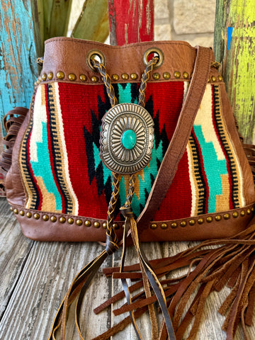 Women’s American Darling bucket fringe concho small bag in brown multi, genuine leather construction with a Southwestern woven textile front and bold turquoise-tone concho accent, measuring 14 x 11 x 4.5 inches – ADBG836A. Available at Blair's Western Wear, Marble Falls, TX.