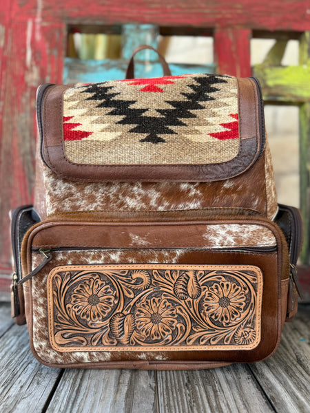 Women’s American Darling cowhide blanket backpack in brown and red, crafted from genuine hair-on hide, with a hand-tooled floral leather pocket and woven wool flap – ADBG1787. Available at Blair’s Western Wear, Marble Falls, TX.