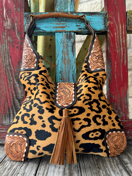 Women's American Darling purse leopard tool hide purse in tan and black, crafted from genuine hair-on hide leather with hand-tooled floral accents, featuring a soft hobo silhouette with secure zipper closure - ADBGA237E. Available at Blair's Western Wear, Marble Falls, TX.